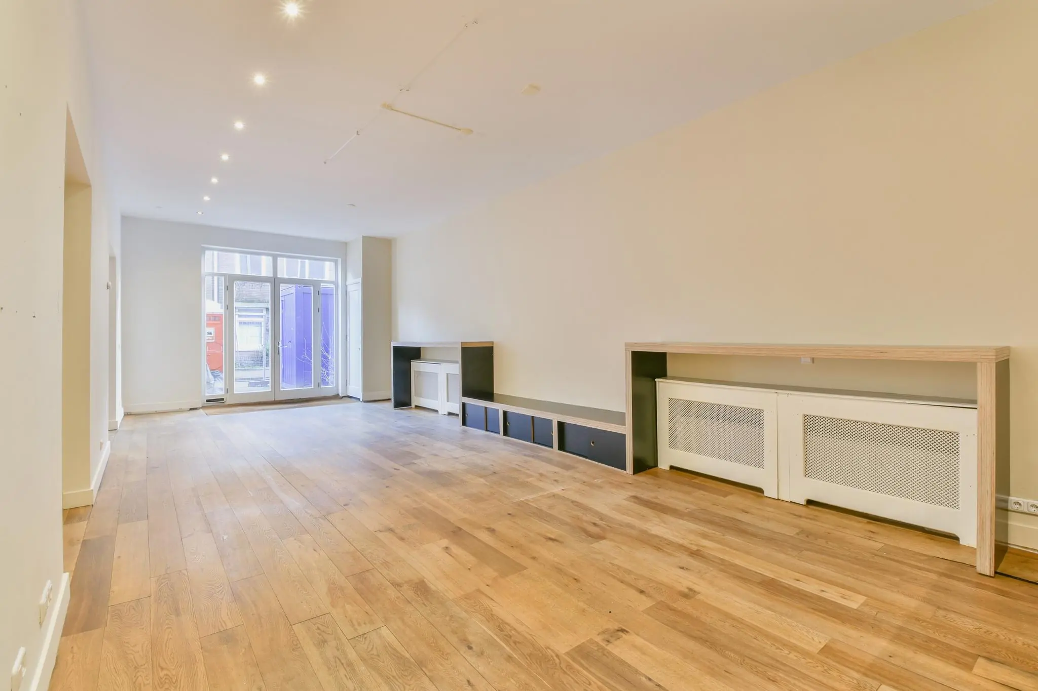 Lichte, lege woonkamer aan de Korte Schimmelstraat met houten vloer, inbouwkasten en grote glazen deuren naar buiten.